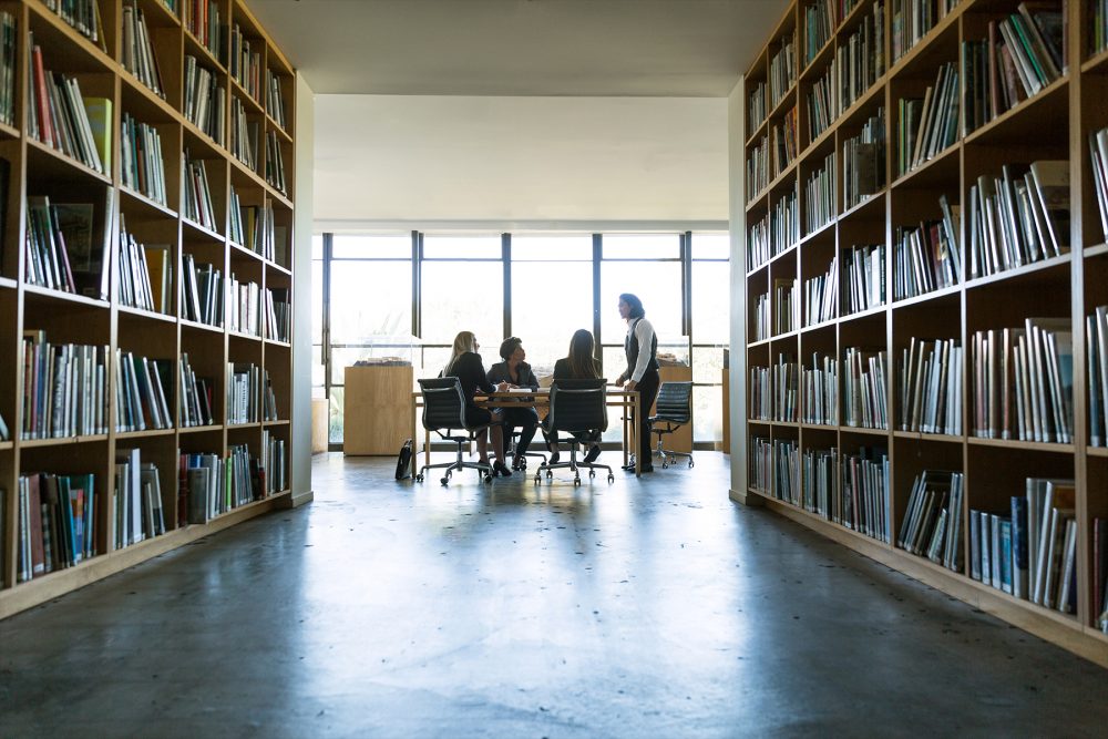 A group of people sitting in a library with bookshelves.