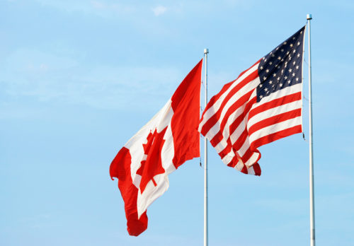 Canadian and American flags flying in the wind.