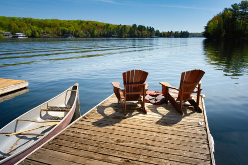 Two Adirondack chairs on a wooden dock facing the blue water of