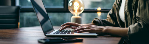 A woman typing on a laptop in front of a light bulb.