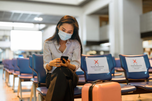 A woman wearing a face mask sitting on a chair at an airport.