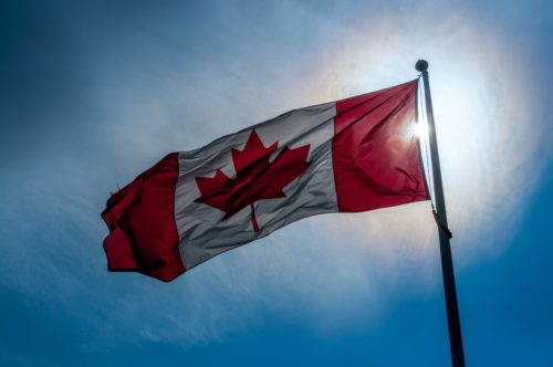 A canadian flag flies in the wind against a blue sky.