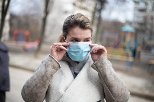 A woman wearing a surgical mask in a park.