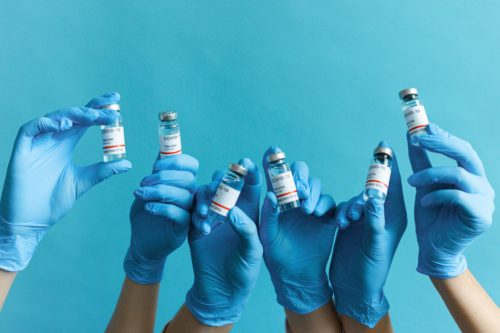 A group of hands holding syringes on a blue background.