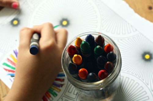 A child is drawing with colored crayons in a jar.