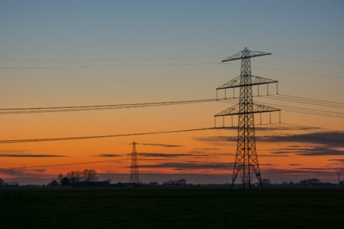High voltage pylons in a field at sunset.