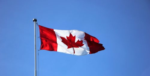 A canadian flag flies in the wind against a blue sky.